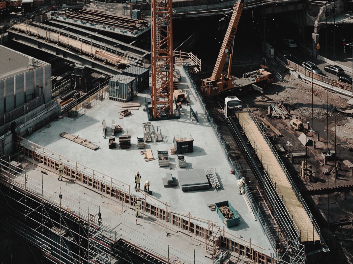 Workers on a newly poured deck of a city construction site, with materials stacked ready and a mobile crane alongside.